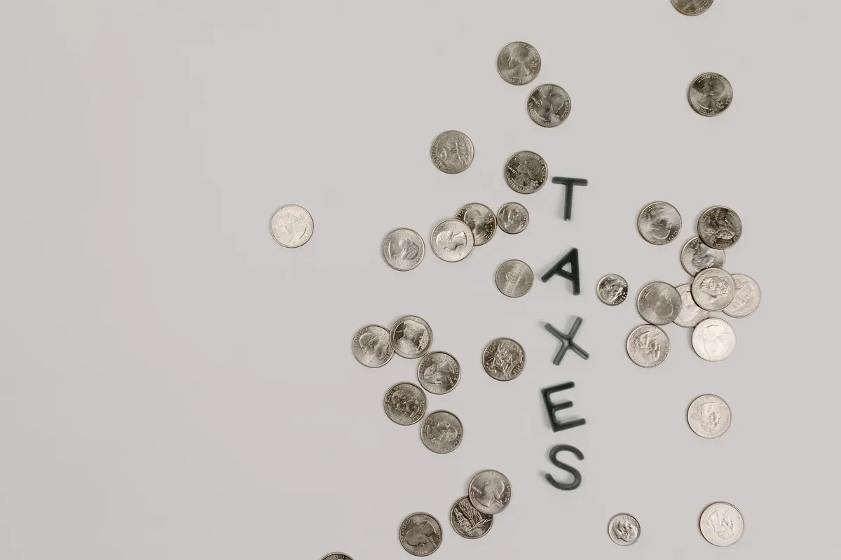 Scattered coins forming the word 'TAXES' on a white surface, symbolizing financial concepts.