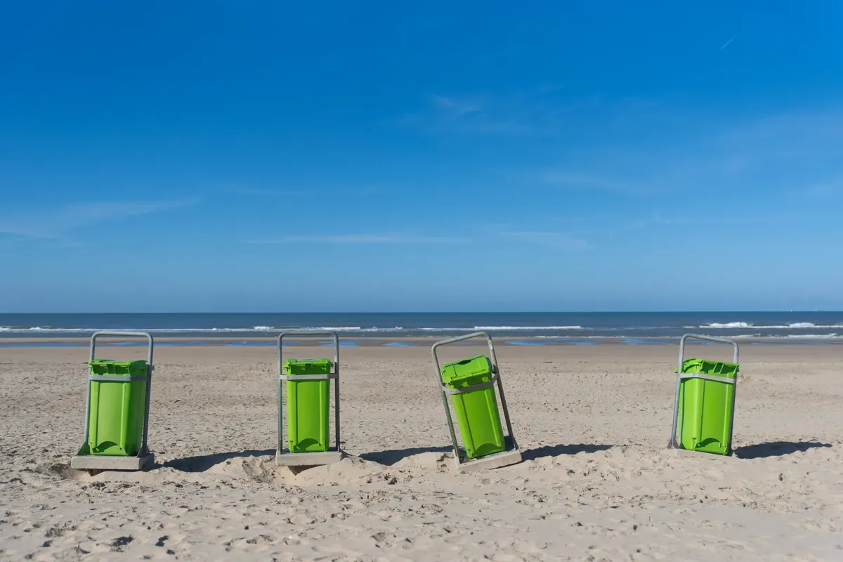 Serene sandy beach with vibrant green trash bins facing the ocean under a clear blue sky.