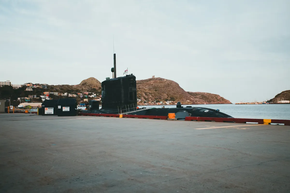 A submarine docked at a pier, surrounded by picturesque hills and calm waters.