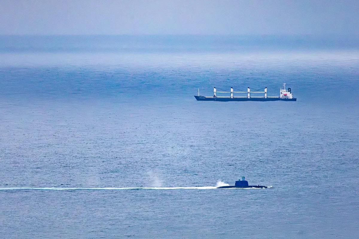 A cargo ship and submarine navigate the vast, open ocean under a clear sky.